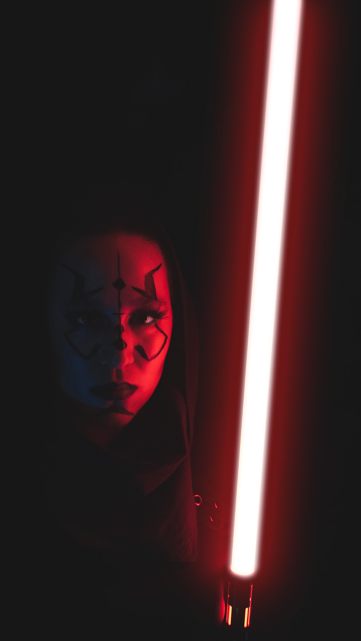 A photo taken by photographer Adam Scott. His model and wife Leslie holds a red lightsaber and half her face is illuminated by the sabers glow.