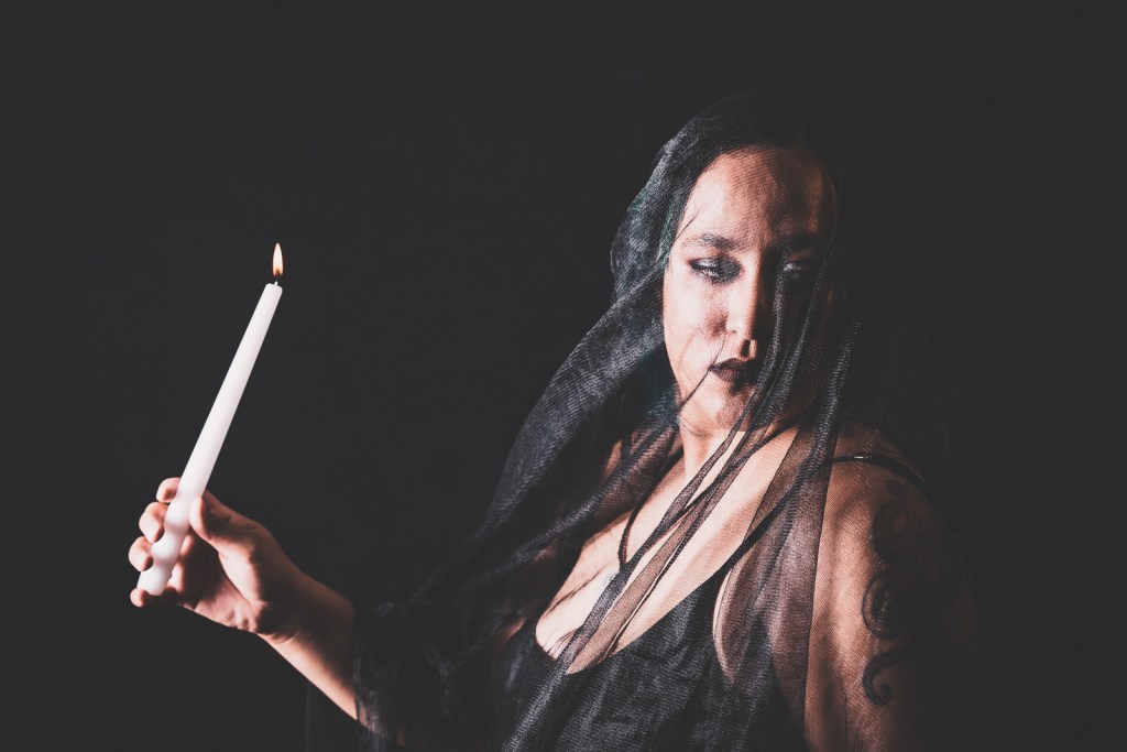An image, taken by photographer Adam Scott. His wife, model, and muse, Leslie Rosado, is posed with a candle while wearing a black shawl.